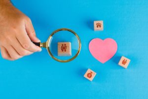family-concept-with-paper-cut-heart-blue-table-flat-lay-hand-holding-magnifying-glass-wooden-cube_176474-9437
