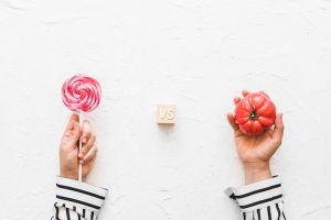 overhead-view-hands-holding-lollipop-versus-red-tomatoes-textured-background_23-2147885720