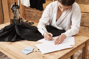 this-piece-clothes-will-be-my-best-side-angle-shot-busy-talented-sewer-creating-design-new-outfit-standing-her-workshop-near-table-with-sewing-machine-fabric-imagination-is-key_176420-14564