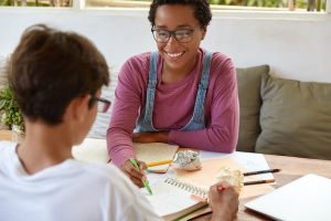 cheerful-teenager-tries-explain-material-younger-brother-who-sits-back-camera_273609-28612