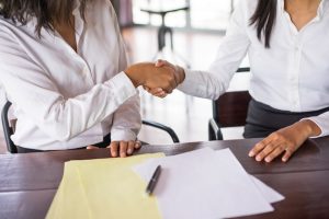 closeup-two-business-women-shaking-hands-sitting-desk_1262-12285