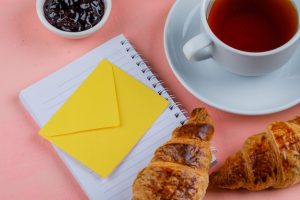 croissant-with-tea-jam-envelope-notebook-close-up-pink-table_176474-8188