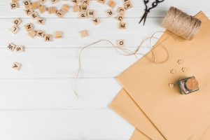 high-angle-view-wooden-text-cube-string-spool-scissor-with-brown-paper-white-table_23-2148193624