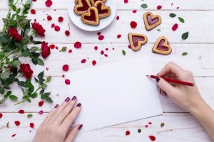 person-drawing-white-paper-with-red-pencil-near-heart-shaped-cookies-with-rose-petals_181624-8580