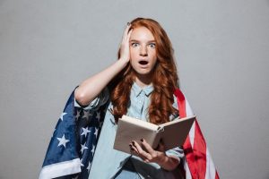 shocked-redhead-young-lady-reading-book-wearing-usa-flag_171337-10737