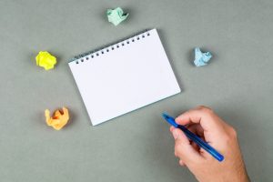 taking-notes-concept-with-notebook-torn-notes-gray-background-top-view-hand-holding-pen-space-text-horizontal-image_176474-6724