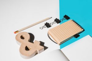 blank-page-ampersand-symbol-spiral-notepad-bulldog-clips-white-blue-background_23-2147907174