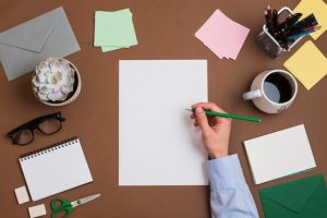 close-up-person-s-hand-writing-white-blank-paper-with-stationeries-desk_23-2147979160-2