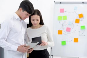 colleagues-looking-digital-tablet-cellphone-standing-near-flipchart_23-2148073249