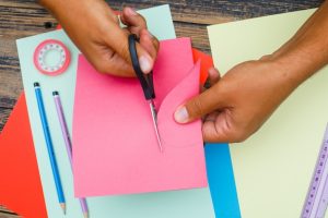 handcraft-concept-with-tools-wooden-background-flat-lay-man-cutting-heart-out-paper_176474-7721