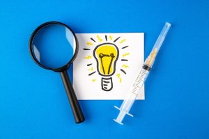 top-view-antivirus-injection-with-magnifier-lightbulb-drawing-blue-surface-hospital-health-virus-covid-pandemic-lab-drug-science_179666-19664-3